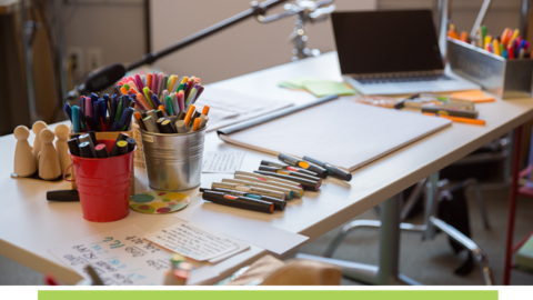 Studio table with markers, drawing pad and laptop.