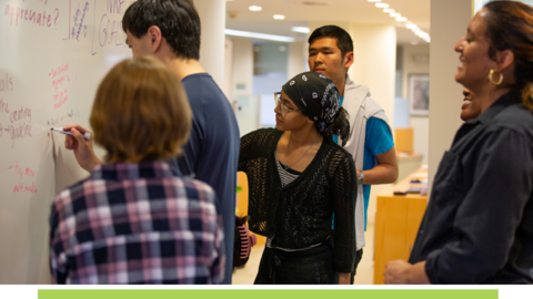 Students standing around a whiteboard.