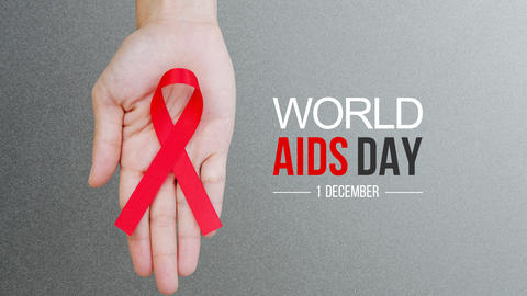 A hand holds a red ribbon, the symbol of HIV/AIDS awareness. World AIDS Day, 1 December.