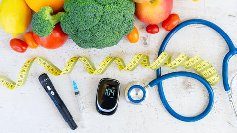 Colorful fruits and vegetables next to a lancet, glucometer, syringe, and stethoscope.