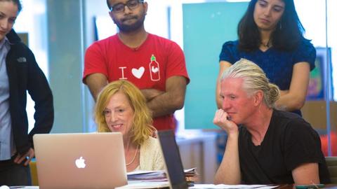 Sue J. Goldie in front of a laptop with meeting attendees looking on.