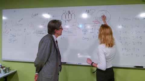 Sue J. Goldie and Julio Frenk drawing on a whiteboard.