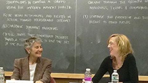 Sue J. Goldie and Paula Johnson sitting in front of classroom.