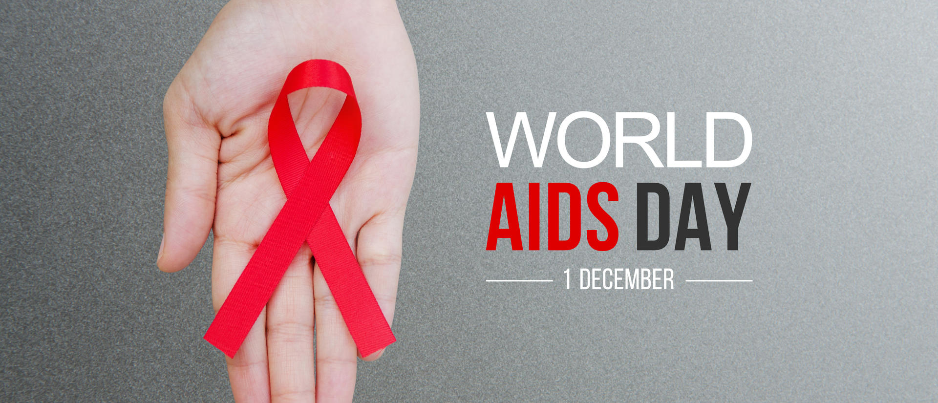 A hand holds a red ribbon, the symbol of HIV/AIDS awareness. World AIDS Day, 1 December.