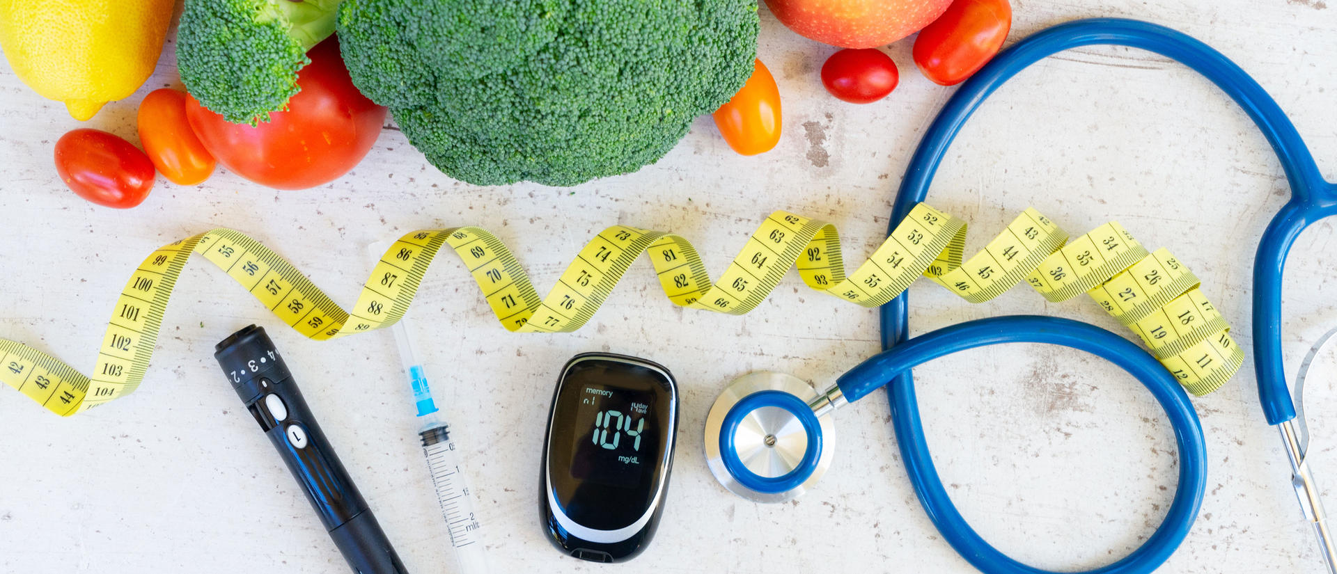 Colorful fruits and vegetables next to a lancet, glucometer, syringe, and stethoscope.